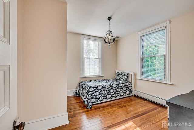 bedroom with baseboard heating, multiple windows, hardwood / wood-style floors, and a chandelier