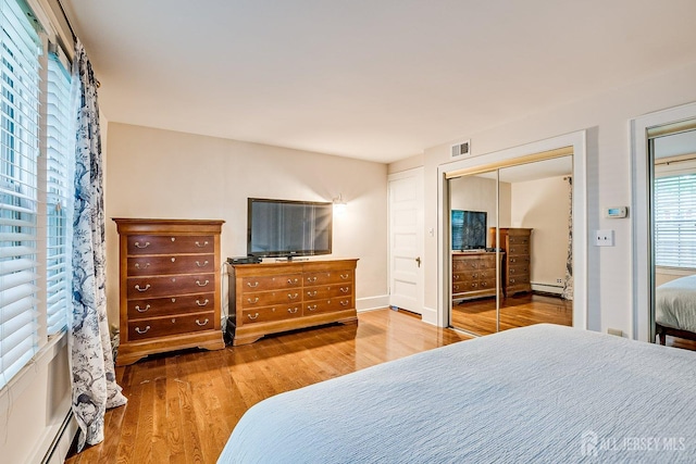 bedroom featuring wood finished floors, baseboard heating, a closet, and a baseboard radiator
