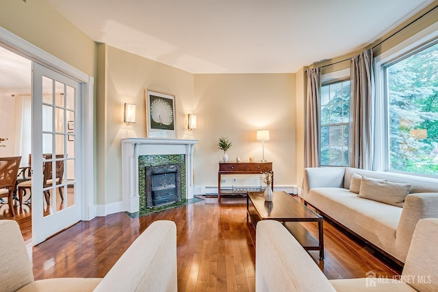living area with baseboard heating, wood-type flooring, a tile fireplace, and baseboards
