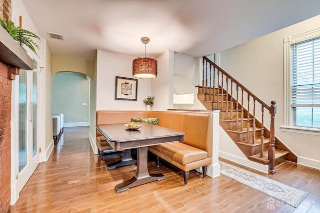 dining room featuring arched walkways, light wood-style floors, baseboards, stairs, and radiator heating unit