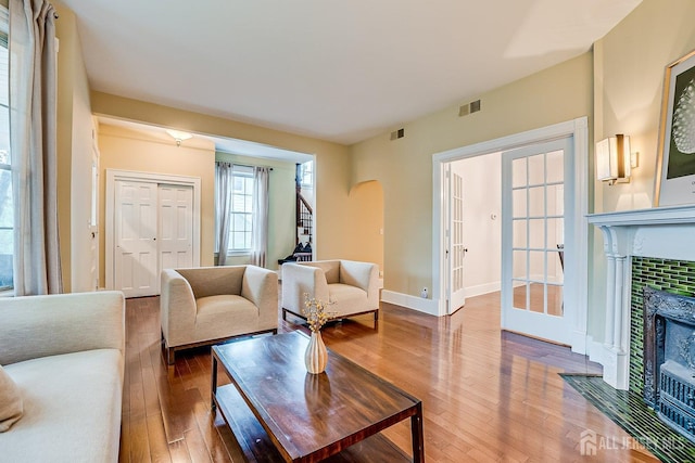living room featuring arched walkways, hardwood / wood-style flooring, a tiled fireplace, and baseboards