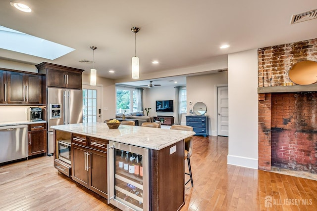 kitchen with appliances with stainless steel finishes, wine cooler, light wood-style flooring, dark brown cabinetry, and pendant lighting