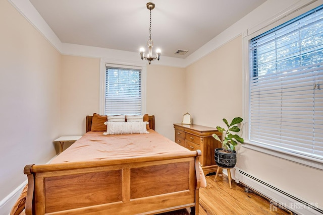 bedroom with a baseboard heating unit, light wood finished floors, and a chandelier
