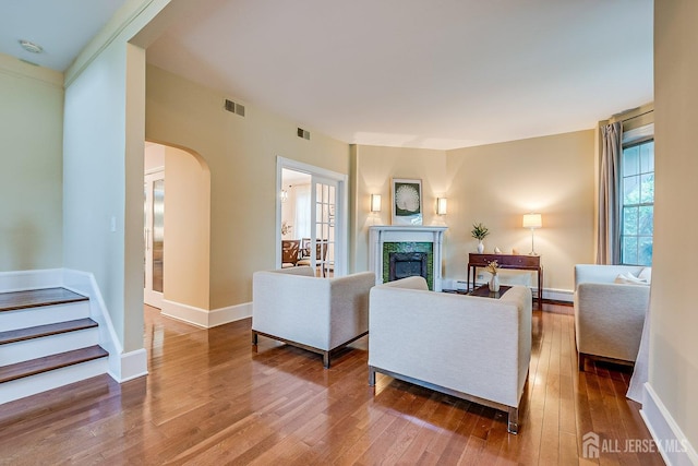 living area with wood-type flooring, a fireplace, arched walkways, a baseboard heating unit, and stairs