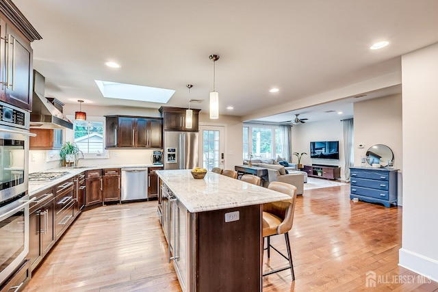 kitchen with stainless steel appliances, a kitchen bar, a skylight, a kitchen island, and wall chimney exhaust hood
