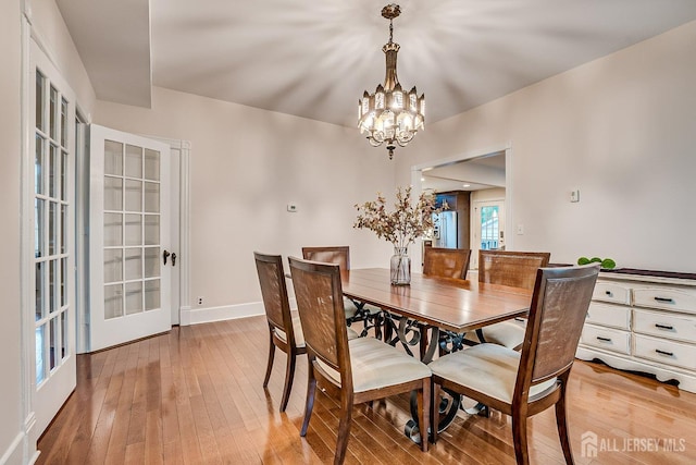 dining space featuring a chandelier, light wood finished floors, baseboards, and french doors