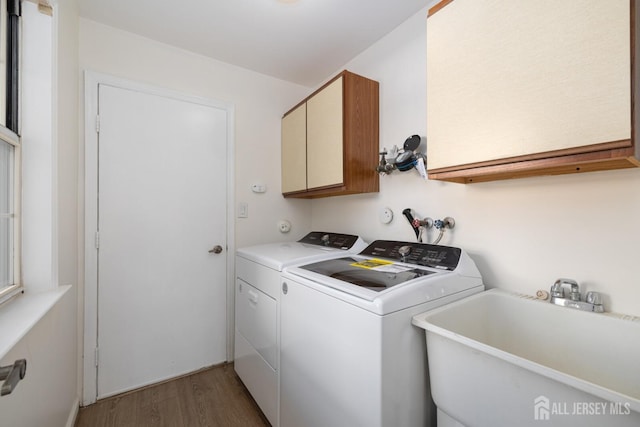 washroom with washing machine and dryer, cabinet space, a sink, and wood finished floors