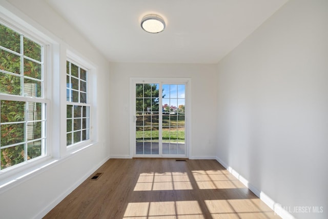 empty room with wood finished floors, visible vents, and baseboards