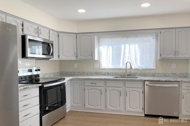 kitchen featuring stainless steel appliances, backsplash, a sink, and light wood-style floors