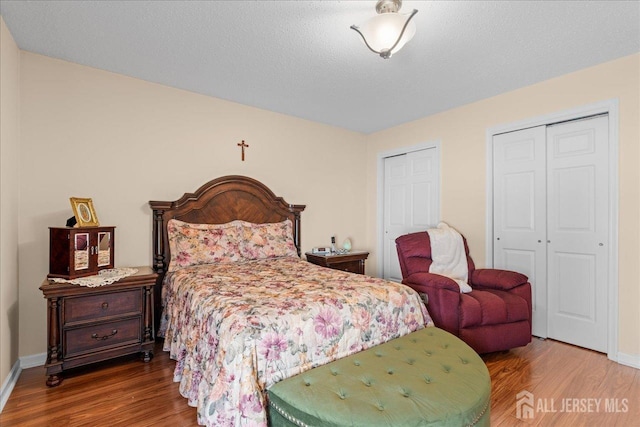 bedroom with wood-type flooring, a textured ceiling, and two closets