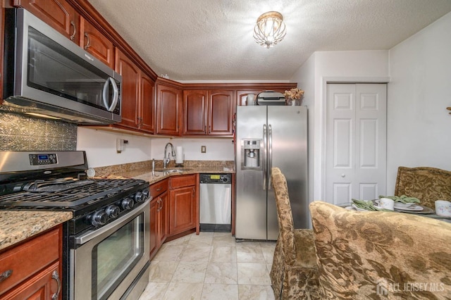 kitchen with light stone countertops, appliances with stainless steel finishes, a textured ceiling, and sink