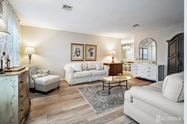 living room featuring a textured ceiling, light hardwood / wood-style flooring, and a chandelier