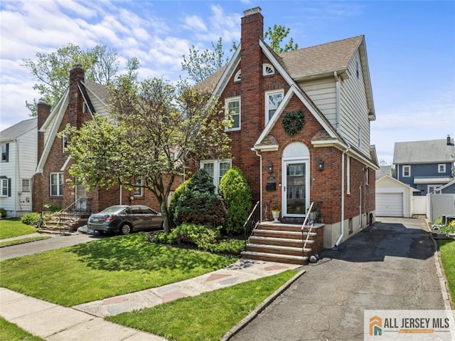 english style home featuring brick siding, an outdoor structure, a front lawn, a chimney, and a detached garage