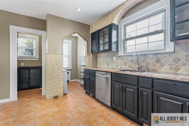 kitchen with stainless steel dishwasher, a sink, arched walkways, glass insert cabinets, and light stone counters