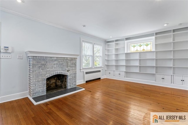 unfurnished living room with radiator heating unit, built in shelves, crown molding, wood-type flooring, and baseboards