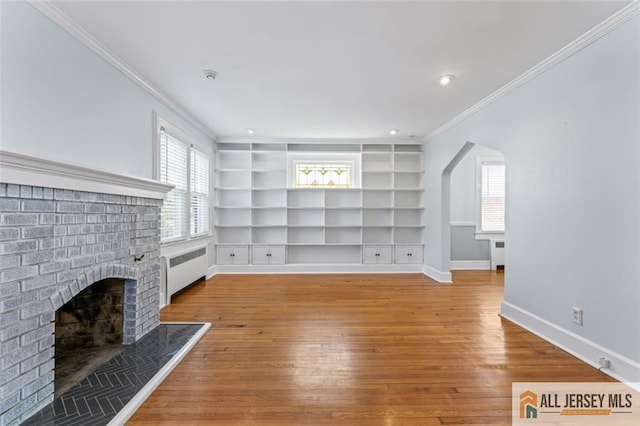 unfurnished living room with radiator, ornamental molding, hardwood / wood-style flooring, baseboards, and a brick fireplace