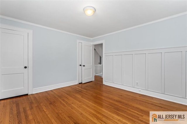 unfurnished room featuring wood finished floors, ornamental molding, and a wainscoted wall