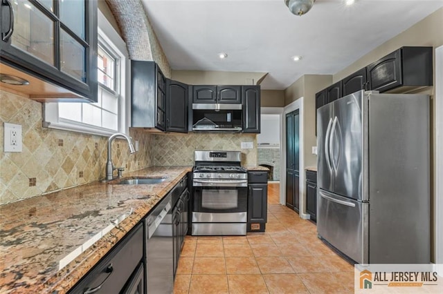 kitchen featuring stainless steel appliances, a sink, light stone countertops, light tile patterned floors, and backsplash