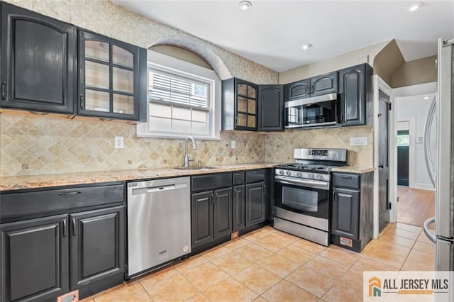 kitchen with appliances with stainless steel finishes, a sink, plenty of natural light, light stone countertops, and recessed lighting