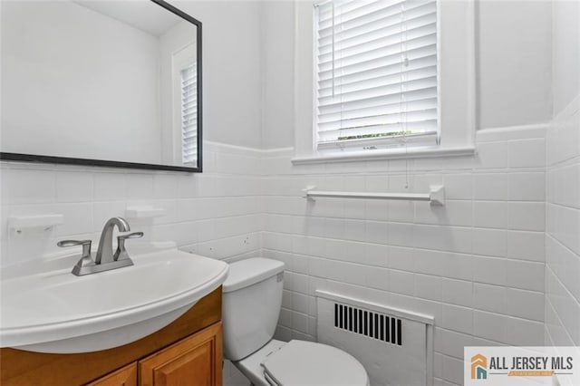 half bathroom featuring radiator heating unit, tile walls, healthy amount of natural light, toilet, and vanity