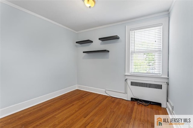 spare room featuring radiator heating unit, wood finished floors, crown molding, and baseboards