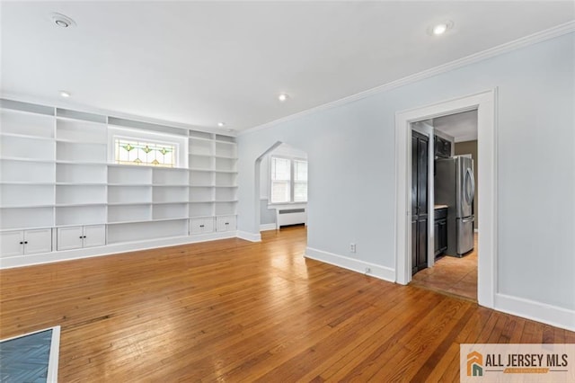 spare room with baseboards, built in shelves, wood-type flooring, radiator heating unit, and arched walkways