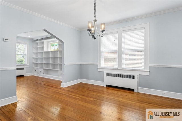 unfurnished dining area featuring radiator heating unit, a chandelier, wood-type flooring, arched walkways, and crown molding