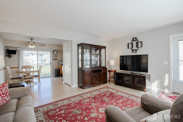 living area featuring light wood-style flooring, a ceiling fan, and baseboards