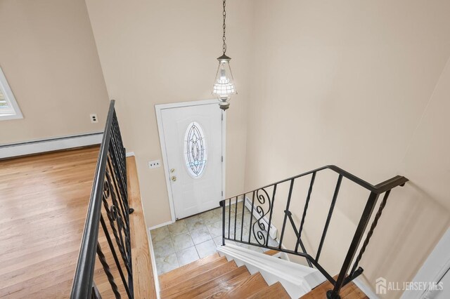 foyer featuring a baseboard radiator, a towering ceiling, and light wood-type flooring