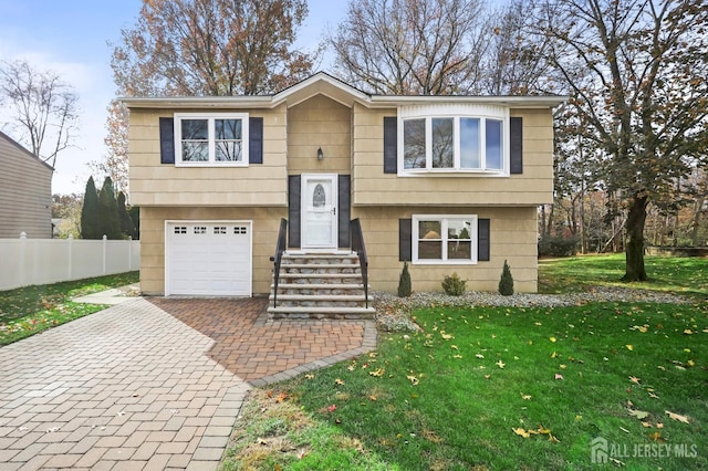 split foyer home with a garage, a front yard, decorative driveway, and fence