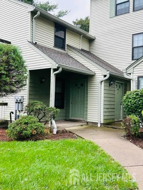 entrance to property with roof with shingles and a lawn