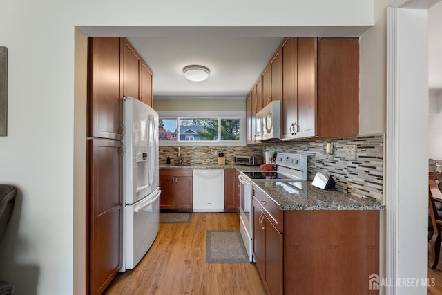 kitchen featuring white appliances, light wood-style floors, a sink, tasteful backsplash, and dark stone countertops