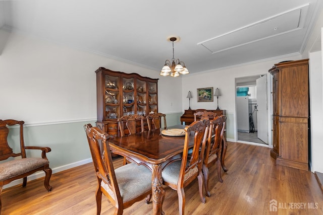 dining area with wood finished floors, attic access, crown molding, baseboards, and a chandelier