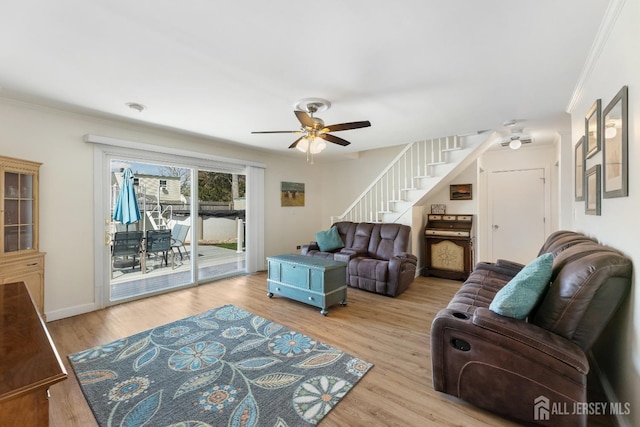 living area with stairway, a ceiling fan, wood finished floors, ornamental molding, and baseboards