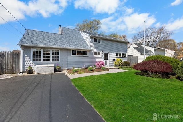 back of property featuring asphalt driveway, an attached garage, a shingled roof, and a chimney