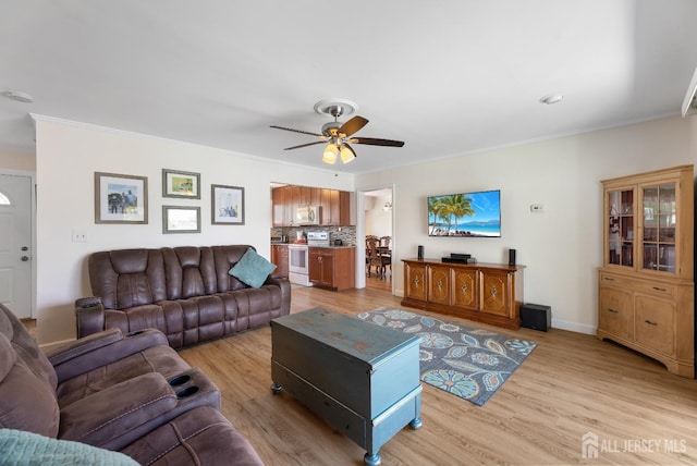 living room featuring ceiling fan, light wood finished floors, crown molding, and baseboards