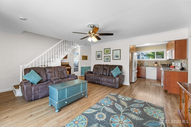 living room featuring light wood-style floors, stairway, ceiling fan, ornamental molding, and baseboards