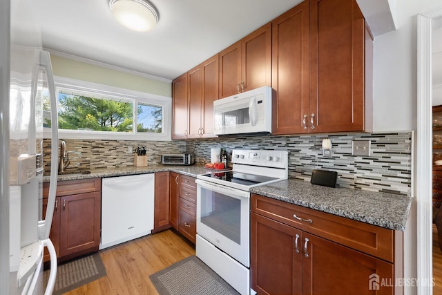 kitchen with white appliances, light wood-style flooring, decorative backsplash, brown cabinetry, and dark stone countertops
