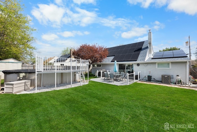 rear view of house featuring a shingled roof, solar panels, an outdoor pool, a yard, and a patio area
