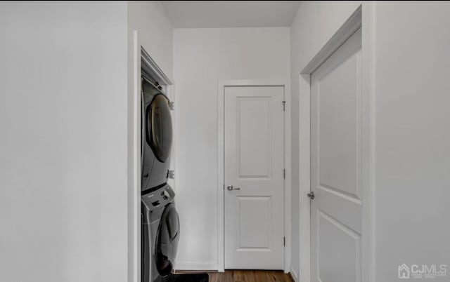 clothes washing area featuring stacked washing maching and dryer, dark wood-style floors, and laundry area