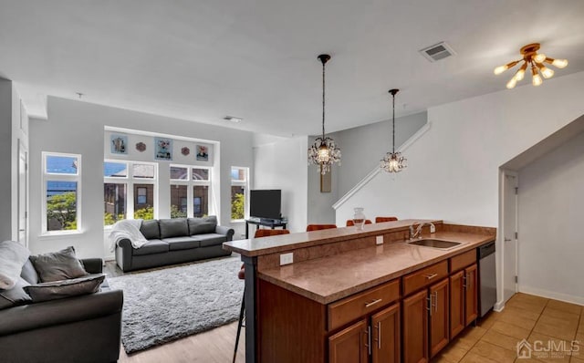 kitchen featuring brown cabinets, a breakfast bar, visible vents, stainless steel dishwasher, and a sink