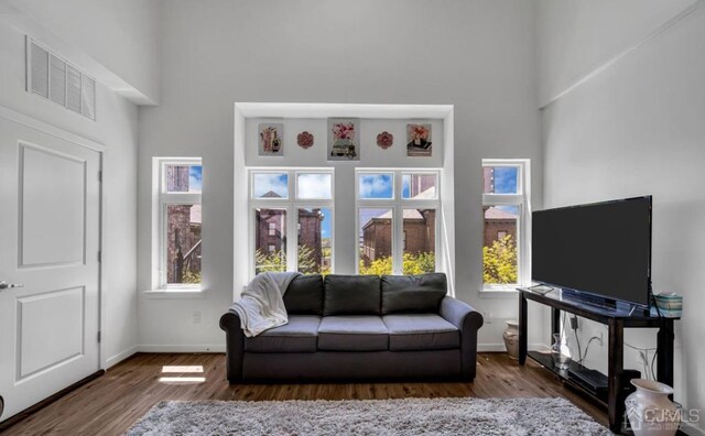 living area featuring baseboards, wood finished floors, visible vents, and a high ceiling