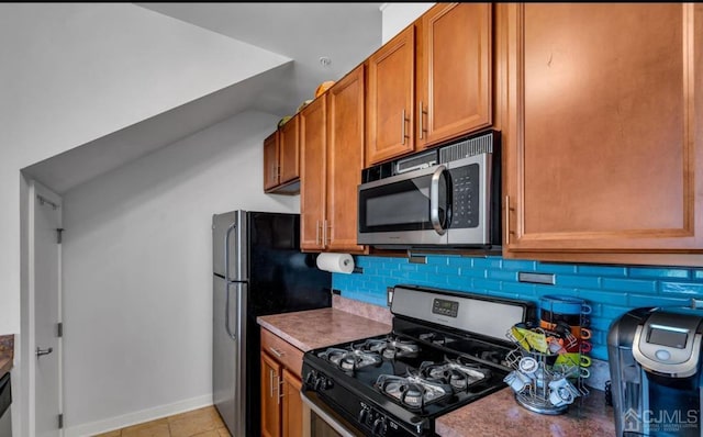 kitchen with vaulted ceiling, brown cabinetry, baseboards, tasteful backsplash, and appliances with stainless steel finishes