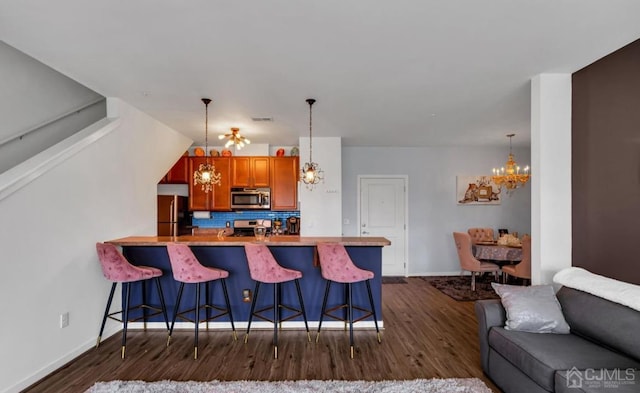 kitchen featuring decorative backsplash, a chandelier, stainless steel appliances, a kitchen bar, and dark wood-style flooring