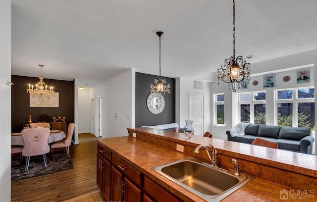 kitchen with wood finished floors, a sink, open floor plan, a chandelier, and decorative light fixtures