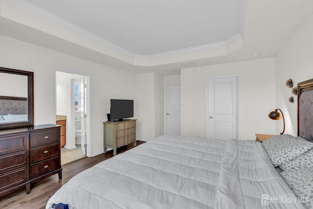 bedroom featuring a raised ceiling, connected bathroom, wood finished floors, and ornamental molding