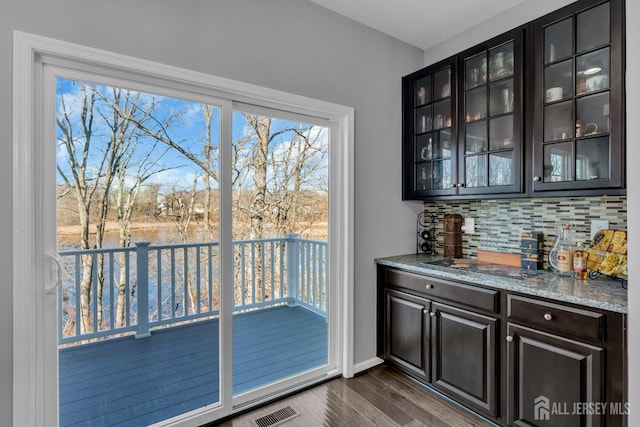 bar featuring a bar, dark wood-type flooring, visible vents, and backsplash