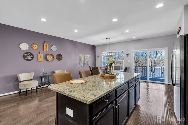 kitchen with dark wood-style floors, a kitchen island, freestanding refrigerator, and light stone countertops