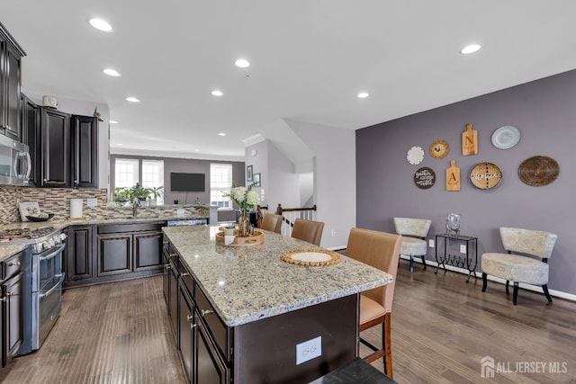 kitchen featuring a center island, light stone countertops, a kitchen bar, appliances with stainless steel finishes, and dark wood-style flooring