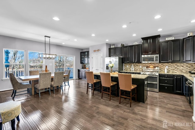 kitchen with backsplash, appliances with stainless steel finishes, a kitchen island, and dark wood-style flooring